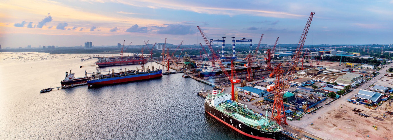 Working port at dusk with berthed carriers, quay cranes and dry dock facilities